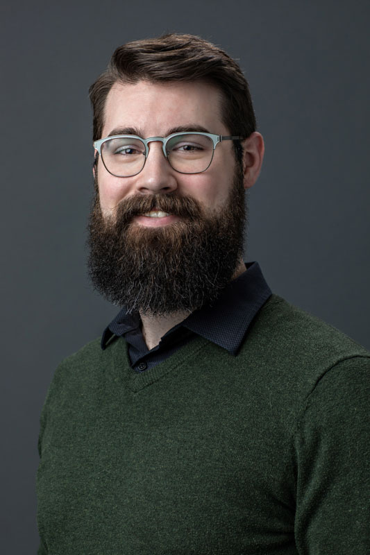 headshot of team member wearing green sweater and beard