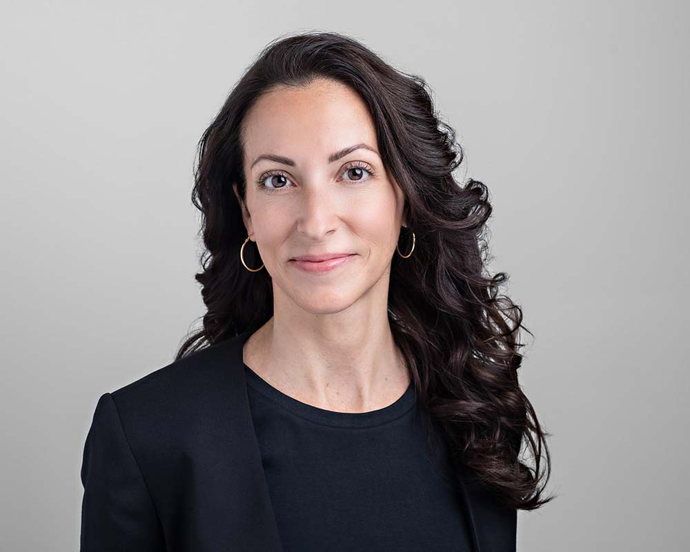 woman with black hair and black outfit posing for executive headshot portrait on grey background