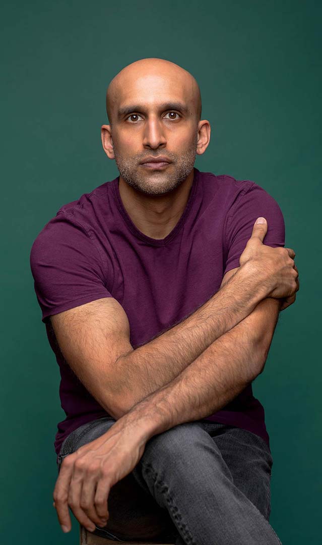 An actor headshot in studio wearing purple shirt on a green seamless background.